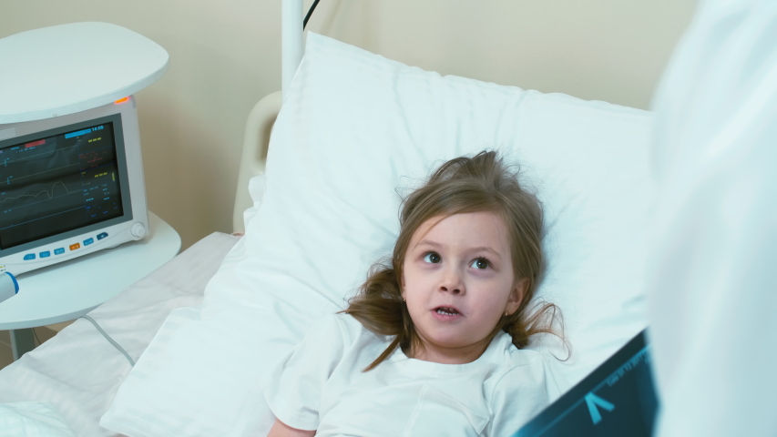 Little girl laying on hospital bed and answering doctors' questions while he examining her X-ray pictures | Shutterstock HD Video #1030826453