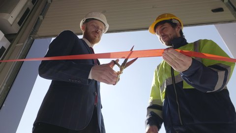 Young entrepreneur and engineer cutting ribbon with scissors. Celebration of opening new industrial factory. Renovation and investments in heavy industry concept