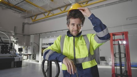 Picture of confident warehouse worker at workplace smiling at camera and putting on hardhat