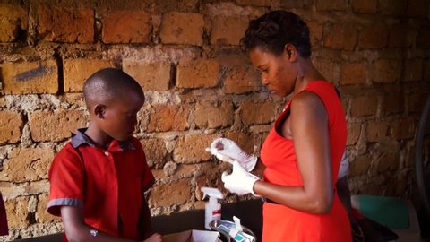Namuwongo, Uganda - 11 01 2017: Medium shot of a african woman in a red dress treating a african boy