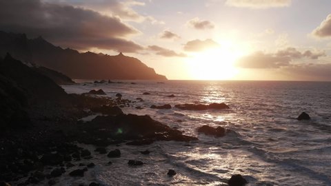 Fantastically beautiful sunset on the north coast of Tenerife, a beach with large stones and black sand. View from above.