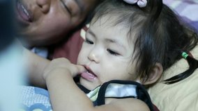 Little Asian baby girl, 2 years old, keeping her thumb in mouth, while the mother reading a bedtime story for her