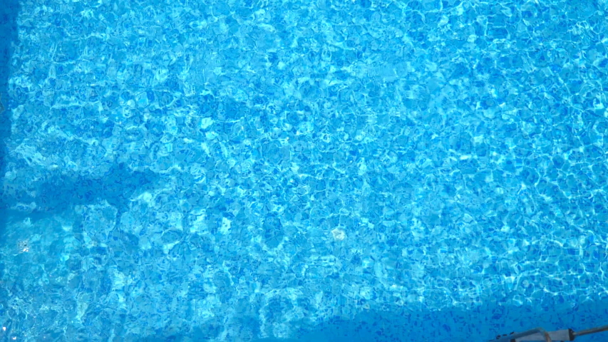 Top view of young man jumping in pool and splashing crystal clear water. Unrecognizable guy swimming under water in basin at sunny day. Boy relaxing during summer vacation. Slow motion Close up