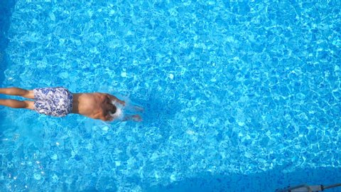 Top view of young man jumping in pool and splashing crystal clear water. Unrecognizable guy swimming under water in basin at sunny day. Boy relaxing during summer vacation. Slow motion Close up