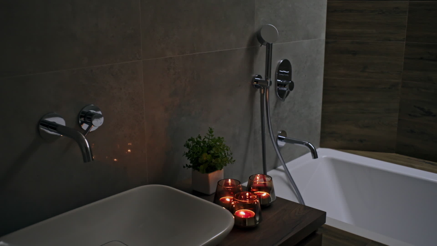 Romantic candlelit bathroom with red burning candles on the vanity, tiled walls and fitted bathtub and basin in timber decor.