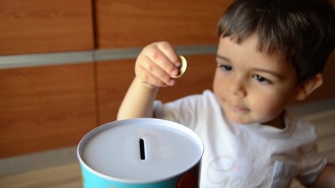 cute two years old saving money, putting coins in metal bank.