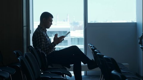 UFA/RUSSIA - 05.05.2019: A man sits in an empty seminar hall or airport. Uses smartphone, rewritten. Waiting for the beginning of the lecture or waiting for the plane.