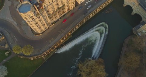Aerial tilts up from Pulteney Bridge and the Avon River to reveal historic centre of Roman city of Bath England UK at sunrise