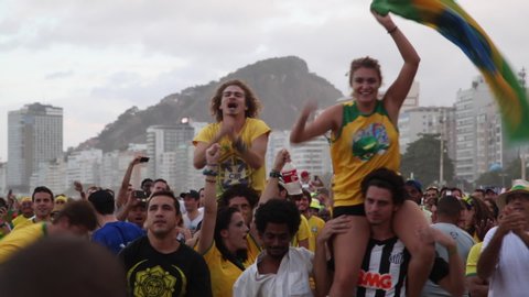 Copacabana, Rio de Janeiro/Brazil - 30th December 2014: Good-looking young millennial male and female Brazilian soccer fans celebrating on friends shoulders in crowd waving national flag