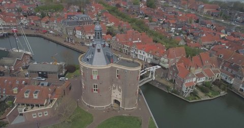 Aerial circling the Drommedaris Defence tower in historic Dutch town Enkhuizen in North Holland the Netherlands with Dutch flag flying revealing the white wooden drawbridge