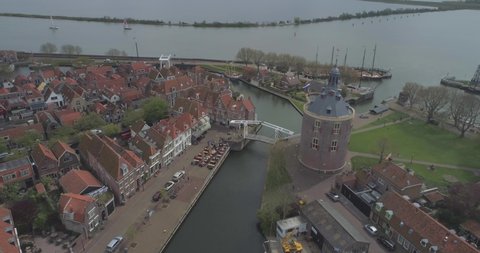 Aerial circling the Drommedaris Defence tower in historic Dutch town Enkhuizen in North Holland the Netherlands with Dutch flag flying traditional houses and rooftops in the background