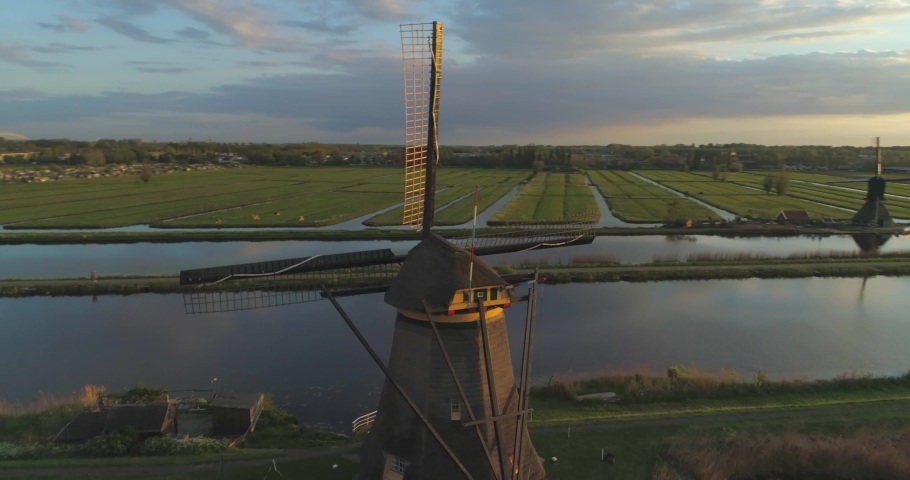 Sunset aerial circling traditional windmill at Kinderdijk UNESCO World heritage site in South Holland, the Netherlands with blades temporarily eclipsing sun in background Royalty-Free Stock Footage #1030886480