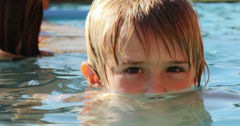 Portrat of small boy child inside swimming pool water looking to camera