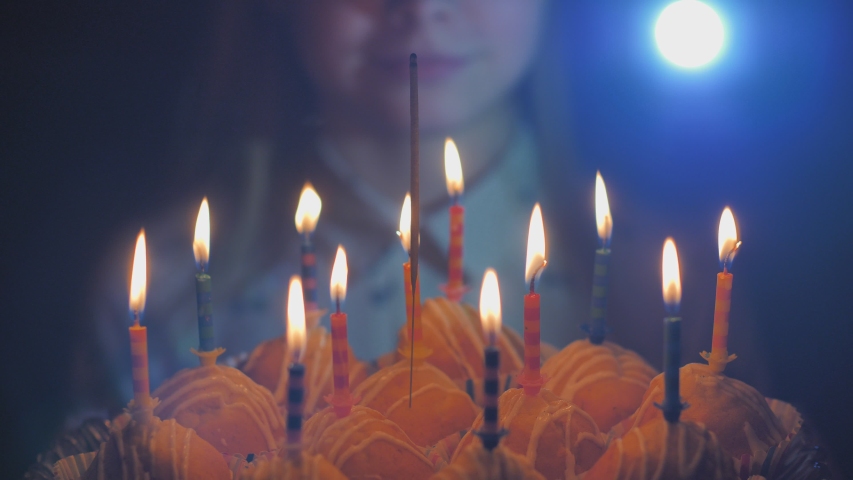 Teen girl admires burning candles at cake on her birthday.