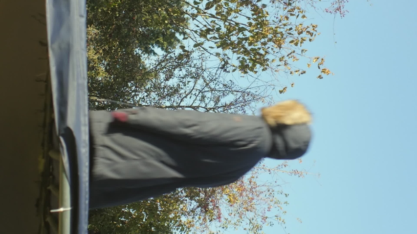 A MEDIUM STATIC SHOT of a young woman jumping on a trampoline. VERTICAL VIDEO.