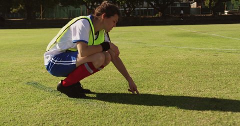 Side view of young Caucasian female soccer player explaining strategy while sitting in squat position on soccer field