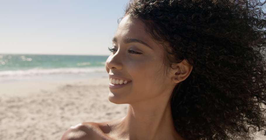 Front view close up of African american woman standing on the beach. She is smiling and looking at camera | Shutterstock HD Video #1030911686