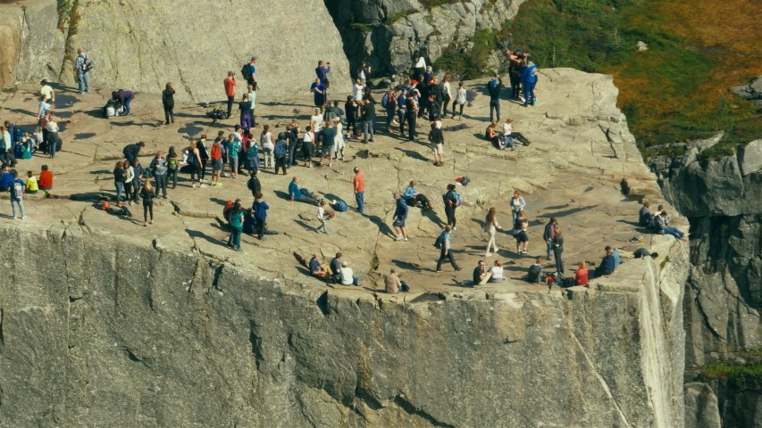 Aerial view from high angle of careless tourists sitting on the edge of Pulpit rock, towering 600 meters above the Lysefjord in Norwegen, taking pictures on cameras and smartphones