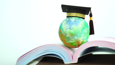 Study abroad education in Global ideas: Graduated cap on top global model on open textbook in library. Concept of studying international educational,reading book bring success degree in life
