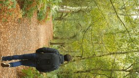 A VERTICAL VIDEO of a man with a big black backpack hiking through the woods.