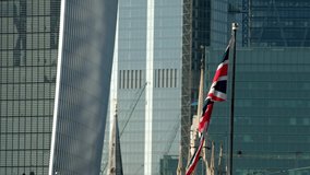Close clip of the Union Jack flying from the bow of HMS Belfast. The background is details of skyscrapers in the City of London