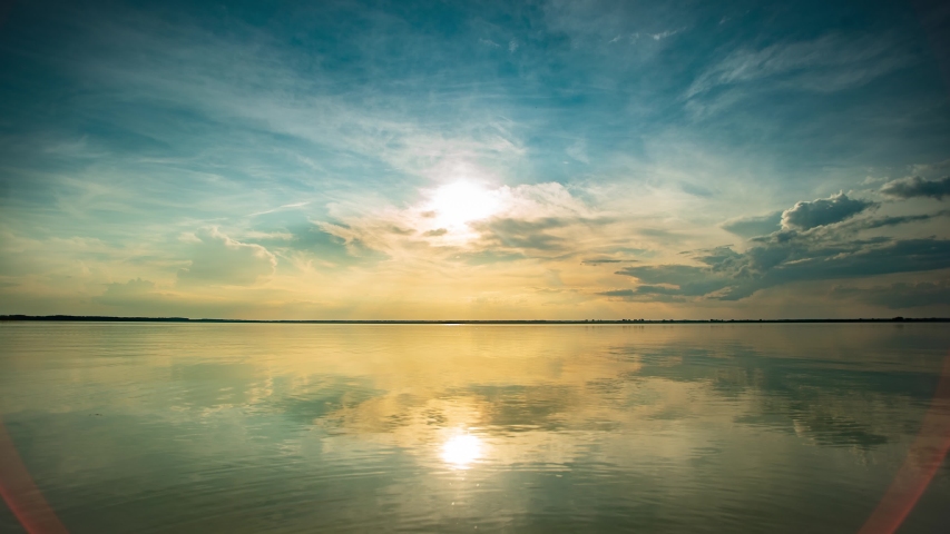 Time lapse Light stretched clouds over evening sky, lake sunset skies. Reflex on flat water