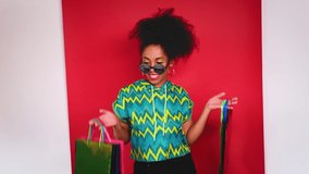 Girl model with lush curly and black hair dancing in the Studio on a red background. In the hands of the girl empty shopping bags. Slow motion. 4K UHD video