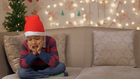 A disappointed little boy sitting alone on a couch for not having received his Christmas gift. Sad and lonely Indian boy waiting for Christmas gift from Santa Claus on Christmas day
