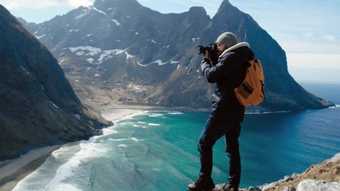 Professional photographer male taking photograph of valley with DSLR wearing backpack photographing scenic landscape nature travel adventure Norway