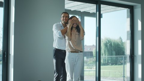 Joyful man closing eyes woman in new home. Happy woman enjoying luxury house. Male person present real estate gift. Couple emotion. Woman surprised emotion. Husband surprising wife with property