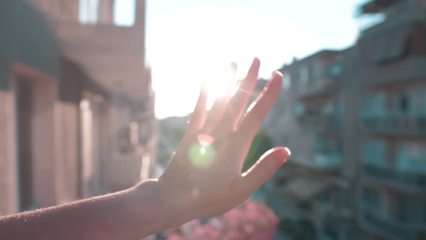 Waving hand to glare of sun flare in afternoon time, urban street. Woman's hand on balcony, sunbeams an gesture. Royalty-Free Stock Footage #1030955726
