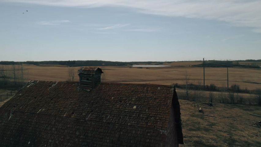 Aerial orbital shot of old barn with decayed tiled roof in farm field