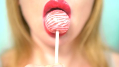 close-up, female sexy lips with red lipstick suck big pink round lollipop. copy space. blue background