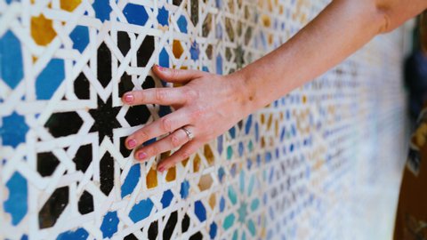 SEVILLE, SPAIN - MAY 9, 2019: Closeup of a hand brushing along ornate colorful mosaic tile pattern in Royal Alcazar