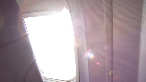 Closeup view of window of airplane with sunlight and sunflares of morning sunrise and part of back of seat. Sunrise time and flying by plane concept. 