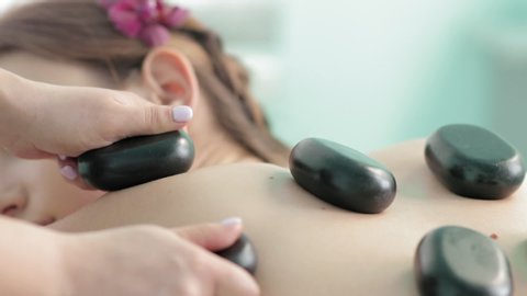 Masseur is doing stone therapy massage to a young woman in spa slow motion