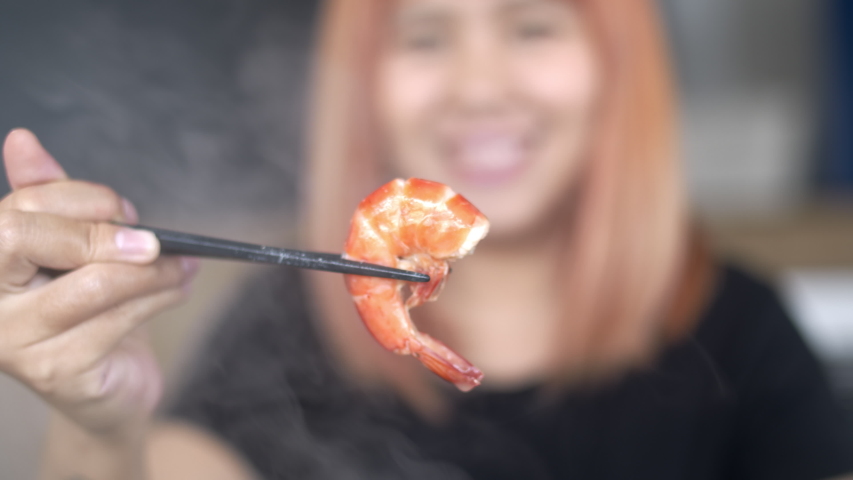 Young Asian woman eating shrimp seafood in restaurant, teenager female feeling happy eating food. Women eating seafood concept. Slow motion shot.