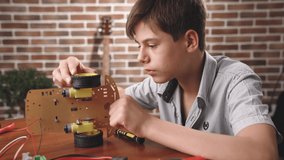 The boy constructs an electronic robot model. Studies design of the model. Very passionate about his work. 4K video with shallow depth of field focus on hands.