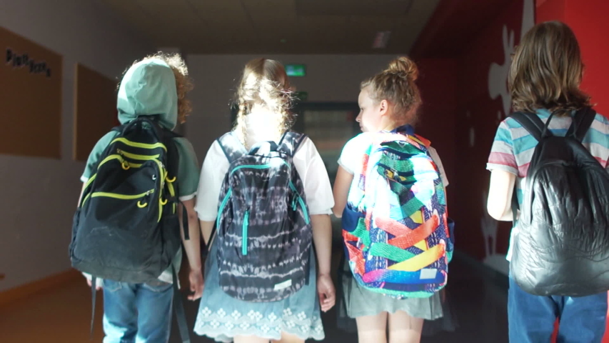 Four schoolchildren of adolescents walk along the school corridor for a lesson. Children go into the dark. Back to school