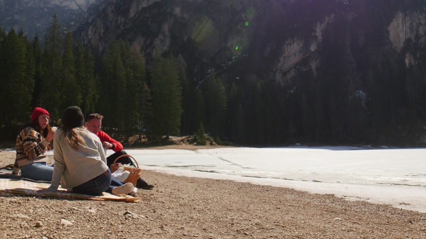 Young people traveling. Friends having a picnic on the coast and eating sandwiches around mountains