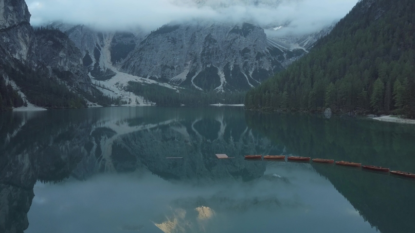 Aerial drone shot in slow motion above the Pragser Wildsee lake with some boats floating on it during a sunny day in South Tyrol, Italy. The camera goes towards the Prags Dolomites.