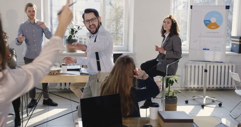 Fun young successful businessman sharing big career success celebration with coworkers doing crazy dance walk at office.