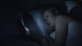A young woman lying in bed at night scrolling on her mobile phone. The bright screen keeping her awake.