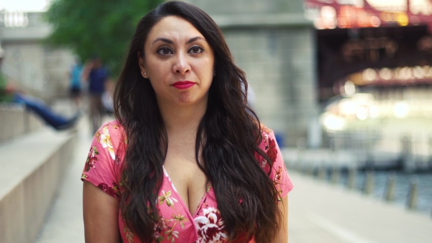Chicago,IL/United States August 18th 2018: Young Latina woman at Chicago River Walk is having an exciting conversation and happy showing many facial expression while moving hair. wearing pink blouse