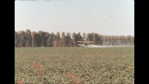 1950s: Crop duster plane sprays field and climbs over treetops.