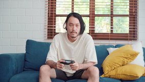 Asian man using joystick playing video games in television in living room, male feeling happy using relax time lying on sofa at home. Men play games relax at home concept.