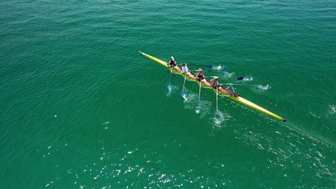 Aerial drone bird's eye view video of yellow sport canoe operated by team of young women in emerald open ocean sea