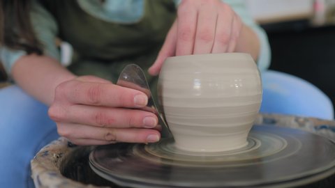 Стоковое видео: Potter gives  a shape to a cup. Girl makes cup out of clay closeup. Twisted potter's wheel. Potter's work close-up. 
Women's hands making clay cup.  