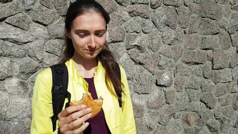 The girl has the hiccups while eating. Funny emotions. A quick snack with a hamburger bun on the street. Dried meat