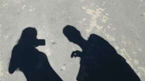 Funny video shadows. Two people wave their hands, build horns on their heads and look at their shadows. Walking in Sunny weather in the city